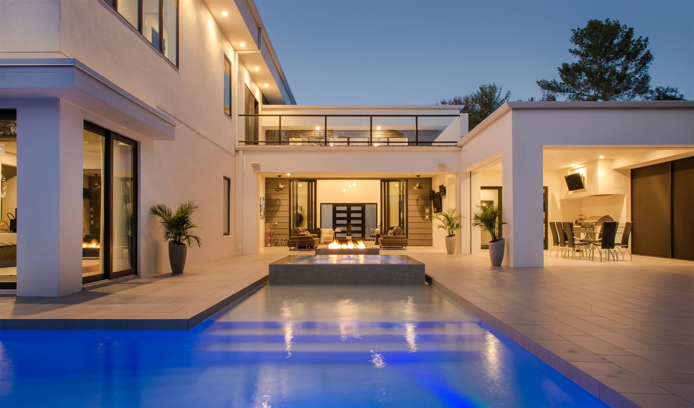 The back of a house at dusk, pool and windows lit